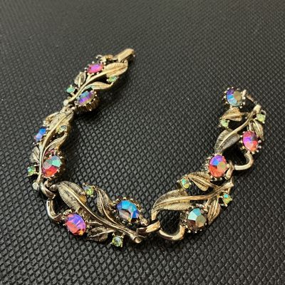 Sale Photo Thumbnail #22: Vintage Coro gold-tone link bracelet featuring textured leaf designs set with colorful, iridescent Aurora Borealis multi-color rhinestones and small accent stones. The fold-over clasp is marked with the Coro copyright logo. Shows light vintage wear consis