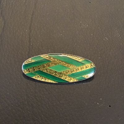 Sale Photo Thumbnail #103: Vintage oval-shaped brooch featuring a geometric gold-tone and green enamel pattern on the front. Measures approximately 1.75 inches long. Features a standard safety pin clasp back. In good vintage condition with minor surface wear consistent with age.