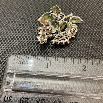 Sale Photo Thumbnail #10: A vintage costume jewelry brooch depicting a cluster of grapes. Features sparkling purple, lavender, and light pink rhinestones representing the fruit, topped with textured green enameled leaves and silver-tone stem detail. Measures approximately 1.5 inch