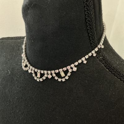 Sale Photo Thumbnail #240: A vintage clear rhinestone choker-style necklace featuring a scalloped drape front design set with round and baguette-cut stones in a silver-tone metal setting. Includes an adjustable hook closure chain. Appears to be in good vintage condition with all st