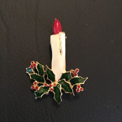 Sale Photo Thumbnail #113: A festive gold-tone Christmas brooch featuring a lit white candle with a red flame, surrounded by dark green enamel holly leaves and red berry accents. Standard pin back mechanism in good working order. Shows light vintage wear with intact enamel. Measure