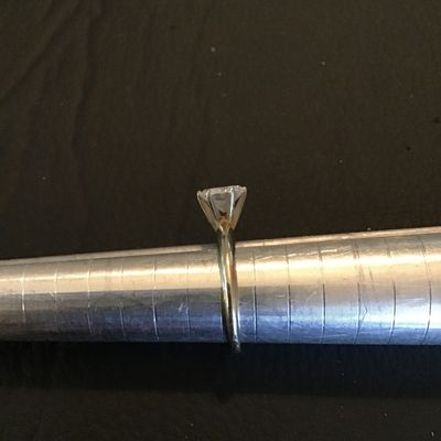 Sale Photo Thumbnail #177: Solitaire style ring featuring a prong-set round brilliant cut clear stone (cubic zirconia or similar crystal/glass). Shown on a ring mandrel measuring approximately size 5.5. Silver-tone metal band. Light wear consistent with use.