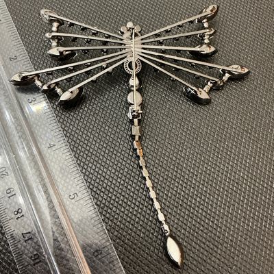 Sale Photo Thumbnail #4: A detailed statement dragonfly brooch set with vibrant blue, iridescent, and green/peridot rhinestones, featuring a light blue cabochon head. Set in dark gunmetal/black-toned metal with a pin back mechanism. Measures approximately 4.5 inches long by 3.5 i