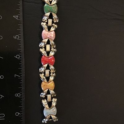 Sale Photo Thumbnail #194: Vintage silver-tone link bracelet featuring colorful textured glass or ceramic cabochons in green, pink, red, yellow, and blue, framed by decorative bow-like metal links. Measures approximately 7 inches in length. Features a fold-over clasp. Good vintage 