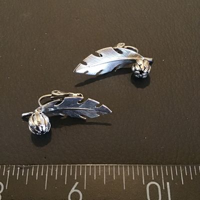 Sale Photo Thumbnail #169: Pair of vintage silver-tone clip-on earrings featuring a textured feather or leaf design with a small detailed flower or acorn accent. Each earring measures approximately 1.5 inches in length. In good vintage condition with working clip backs.