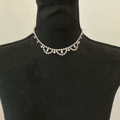Sale Photo Thumbnail #237: A vintage clear rhinestone choker-style necklace featuring a scalloped drape front design set with round and baguette-cut stones in a silver-tone metal setting. Includes an adjustable hook closure chain. Appears to be in good vintage condition with all st
