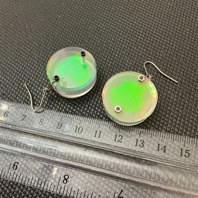 Sale Photo Thumbnail #170: Pair of vintage round clear acrylic/lucite drop earrings featuring a bright green shell motif with an iridescent holographic effect. Fitted with French wire hooks and miniature metal hardware fasteners. Each round charm measures approximately 1 inch in di