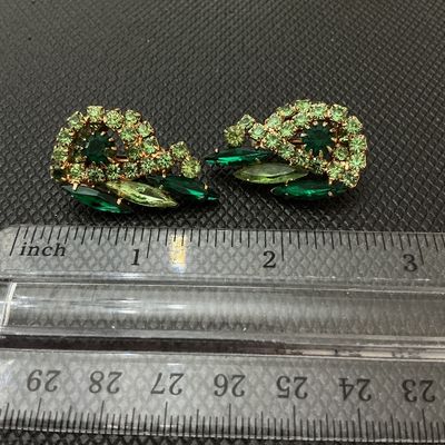 Sale Photo Thumbnail #61: Pair of vintage gold-tone clip-on earrings featuring multi-shade green rhinestones in swirl and marquise cuts. Measure approximately 1.25 inches long. Signed 'Judy Lee' on the clips. Light wear consistent with age, stones remain bright and intact.