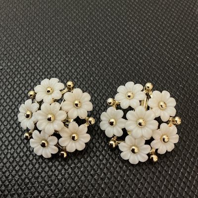 Sale Photo Thumbnail #38: Pair of vintage floral clip-on earrings featuring white molded plastic/lucite flower petals cluster-set around gold-tone center beads and frame. Each earring measures approximately 1 inch in diameter. In good condition with light wear consistent with age;