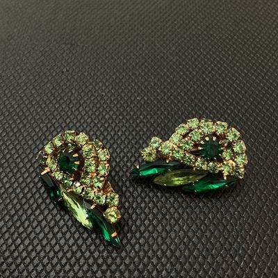 Sale Photo Thumbnail #58: Pair of vintage gold-tone clip-on earrings featuring multi-shade green rhinestones in swirl and marquise cuts. Measure approximately 1.25 inches long. Signed 'Judy Lee' on the clips. Light wear consistent with age, stones remain bright and intact.