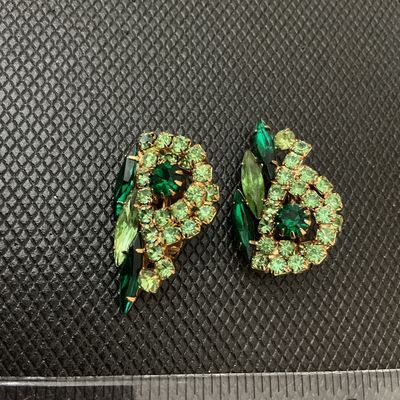 Sale Photo Thumbnail #65: Pair of vintage gold-tone clip-on earrings featuring multi-shade green rhinestones in swirl and marquise cuts. Measure approximately 1.25 inches long. Signed 'Judy Lee' on the clips. Light wear consistent with age, stones remain bright and intact.