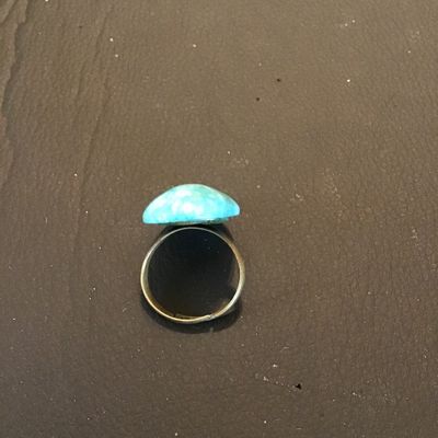 Sale Photo Thumbnail #141: Adjustable costume ring featuring a brass-tone band set with a large oval blue mottled stone or cabochon (turquoise-style appearance). Appears to be in good pre-owned condition with minor surface wear to the metal band.