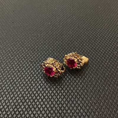 Sale Photo Thumbnail #201: Pair of vintage gold-tone clip-on earrings featuring starburst or textured sunburst frames set with vibrant red/ruby-colored faceted round stones. Each earring measures approximately 1 cm wide according to the ruler shown. Good condition with light wear.