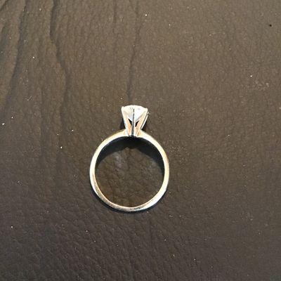 Sale Photo Thumbnail #179: Solitaire style ring featuring a prong-set round brilliant cut clear stone (cubic zirconia or similar crystal/glass). Shown on a ring mandrel measuring approximately size 5.5. Silver-tone metal band. Light wear consistent with use.