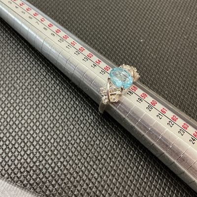 Sale Photo Thumbnail #176: A silver-tone ring featuring a central oval light blue gemstone (possibly topaz) flanked by clear accent stones set in a crisscross bypass design band. Measures approximately size 8 on a ring mandrel. Pre-owned condition with light surface wear.
