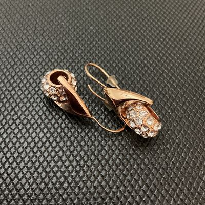 Sale Photo Thumbnail #192: Pair of rose gold-tone drop wire earrings featuring curved leaf-like wraps set with pave rhinestones/crystals. Includes plastic safety backings. Overall length measures approximately 2.5 cm (1 inch) as shown against ruler. Good pre-owned condition with al