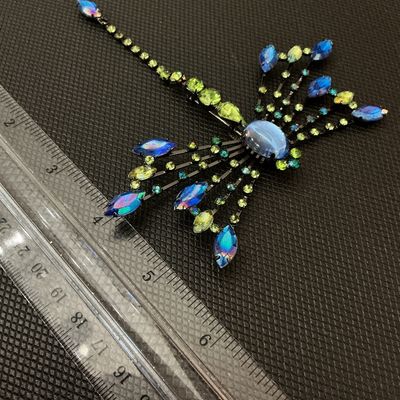 Sale Photo Thumbnail #3: A detailed statement dragonfly brooch set with vibrant blue, iridescent, and green/peridot rhinestones, featuring a light blue cabochon head. Set in dark gunmetal/black-toned metal with a pin back mechanism. Measures approximately 4.5 inches long by 3.5 i