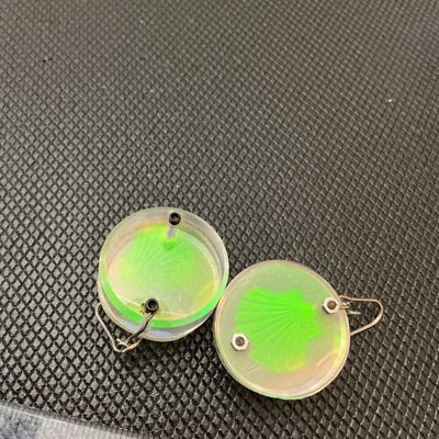 Sale Photo Thumbnail #168: Pair of vintage round clear acrylic/lucite drop earrings featuring a bright green shell motif with an iridescent holographic effect. Fitted with French wire hooks and miniature metal hardware fasteners. Each round charm measures approximately 1 inch in di
