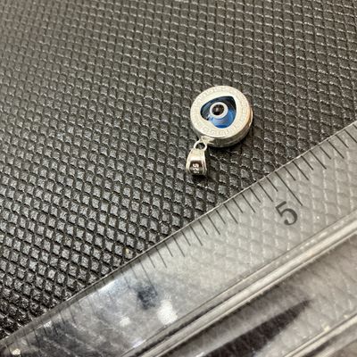 Sale Photo Thumbnail #7: A small sterling silver pendant featuring a central blue glass heart-shaped evil eye (nazar) detail surrounded by a Greek key border motif. The bail is stamped '925' indicating sterling silver content. Measures approximately 1/2 inch in diameter (excludin