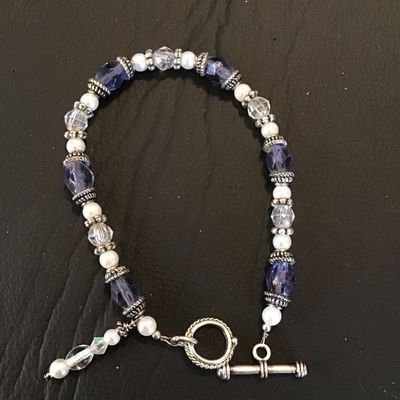 Sale Photo Thumbnail #70: A beaded costume bracelet featuring alternating faceted purple glass or crystal beads, faceted clear glass beads, small faux pearls, and textured metal spacer beads. It fastens with a silvertone rope-texture toggle clasp and includes a short decorative da