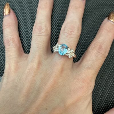 Sale Photo Thumbnail #173: A silver-tone ring featuring a central oval light blue gemstone (possibly topaz) flanked by clear accent stones set in a crisscross bypass design band. Measures approximately size 8 on a ring mandrel. Pre-owned condition with light surface wear.