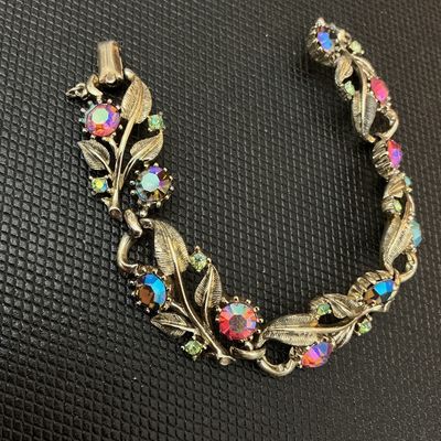 Sale Photo Thumbnail #25: Vintage Coro gold-tone link bracelet featuring textured leaf designs set with colorful, iridescent Aurora Borealis multi-color rhinestones and small accent stones. The fold-over clasp is marked with the Coro copyright logo. Shows light vintage wear consis