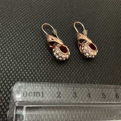 Sale Photo Thumbnail #198: Pair of rose gold-tone drop wire earrings featuring curved leaf-like wraps set with pave rhinestones/crystals. Includes plastic safety backings. Overall length measures approximately 2.5 cm (1 inch) as shown against ruler. Good pre-owned condition with al