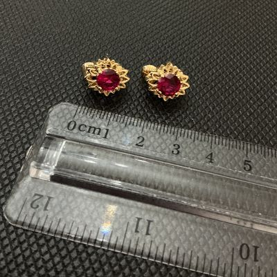 Sale Photo Thumbnail #205: Pair of vintage gold-tone clip-on earrings featuring starburst or textured sunburst frames set with vibrant red/ruby-colored faceted round stones. Each earring measures approximately 1 cm wide according to the ruler shown. Good condition with light wear.