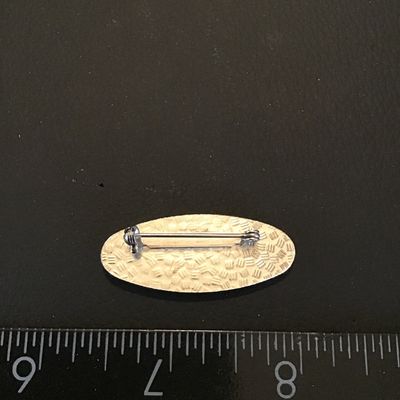 Sale Photo Thumbnail #106: Vintage oval-shaped brooch featuring a geometric gold-tone and green enamel pattern on the front. Measures approximately 1.75 inches long. Features a standard safety pin clasp back. In good vintage condition with minor surface wear consistent with age.