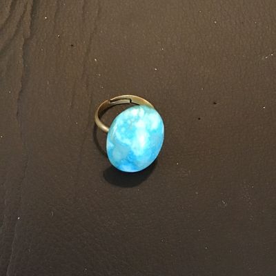 Sale Photo Thumbnail #135: Adjustable costume ring featuring a brass-tone band set with a large oval blue mottled stone or cabochon (turquoise-style appearance). Appears to be in good pre-owned condition with minor surface wear to the metal band.