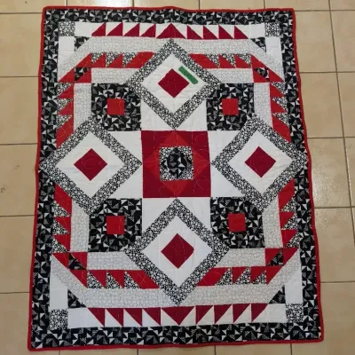 Sale Photo Thumbnail #23: Handmade patchwork quilt featuring geometric diamond and triangle patterns in red, black, and white fabric with a red border.