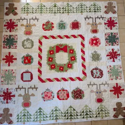 Sale Photo Thumbnail #44: Handcrafted Christmas themed quilt featuring appliquéd and pieced motifs including reindeers, gingerbread men, wreaths, and ornaments on a white tiled floor.