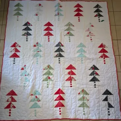 Sale Photo Thumbnail #2: Handmade Christmas tree quilt featuring patterned triangular pine trees on a white background with a red trimmed edge.