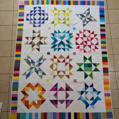 Sale Photo Thumbnail #5: Handmade patchwork quilt featuring geometric star quilt blocks in vibrant colors set against a white background, framed by a colorful piano key border.