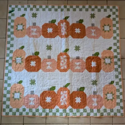 Sale Photo Thumbnail #50: Handcrafted autumn pumpkin patchwork quilt featuring orange and green star-block patterns with a checkerboard border, displayed on a tiled floor.