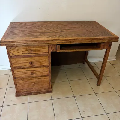 Sale Photo Thumbnail #53: Oak finished wooden desk featuring four stacked side drawers, wooden knobs, and a center keyboard tray.