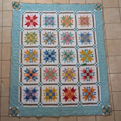 Sale Photo Thumbnail #9: Handmade patchwork quilt with a light blue border and colorful star motif blocks. Appears to be in clean, well-maintained condition.