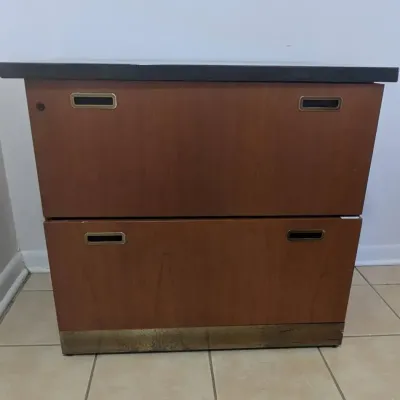 Sale Photo Thumbnail #31: Mid-century modern two-drawer lateral filing cabinet with wood veneer cladding, brass recessed pulls, and a black laminate top.