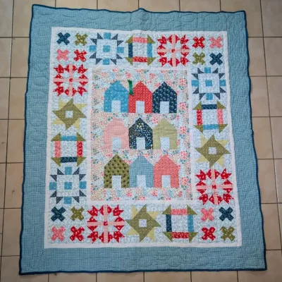 Sale Photo Thumbnail #14: Handmade patchwork quilt featuring a center panel of colorful houses surrounded by a sampler block border and a light blue patterned frame.
