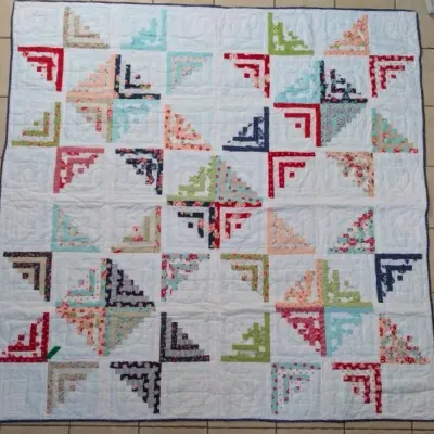 Sale Photo Thumbnail #11: Handmade log cabin pattern quilt with colorful floral and geometric fabric strips on a white quilted background.