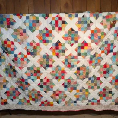 Sale Photo Thumbnail #49: Handmade patchwork quilt featuring a colorful X-and-square pattern set against white fabric with a light patterned border.