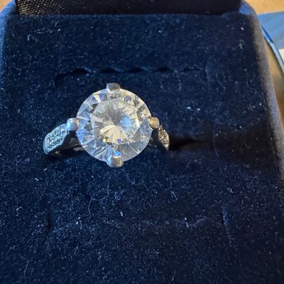 Solitaire ring featuring a large round brilliant-cut center stone set in a four-prong mounting, presented inside a dark velvet ring box.