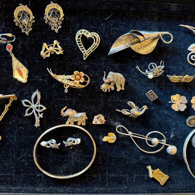 Collection of vintage costume jewelry displayed on a black velvet tray, including sterling silver brooches, clip-on earrings, bangles,...