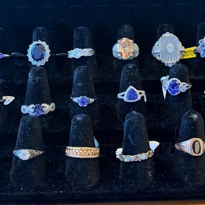 Black velvet ring display tray filled with assorted vintage and modern fine jewelry rings, featuring sapphires, tanzanites, diamonds, and...