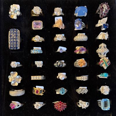 A jewelry display tray filled with an assortment of vintage and modern rings featuring various gemstones, pearls, and diamonds set in...