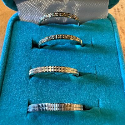 Set of four diamond-cut metal stackable rings or bands displayed inside a teal velvet jewelry box.