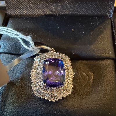 Cushion-cut purple gemstone pendant surrounded by a double halo of round and baguette-cut accent stones, displayed in a black jewelry box.