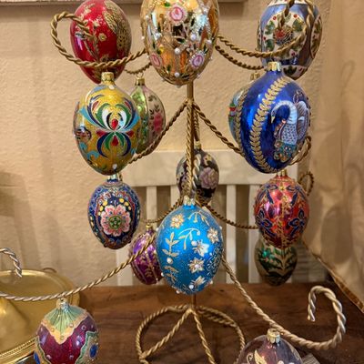 Collection of ornate, hand-painted Faberge-style glass egg ornaments displayed on a brass twisted-wire ornament tree.