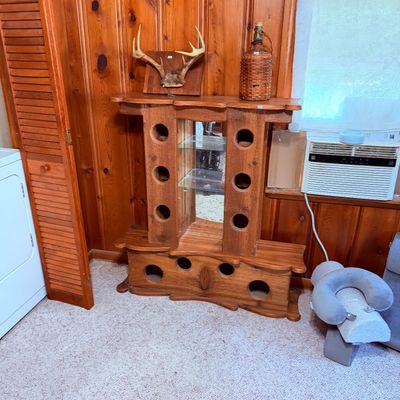 Sale Photo Thumbnail #78: Rustic wooden display unit with circular cutouts and glass shelves, a mounted deer antler taxidermy plaque and wicker-wrapped bottle.