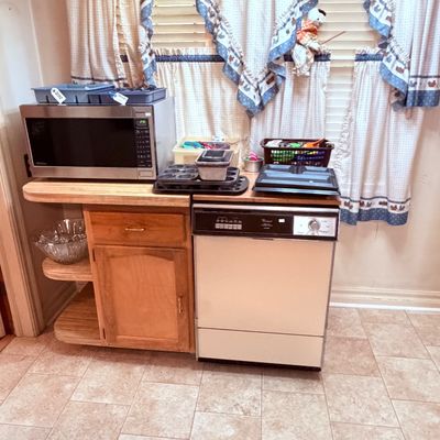 Sale Photo Thumbnail #69: Portable Whirlpool dishwasher alongside a wooden kitchen cart topped with a Panasonic microwave, baking pans, and various kitchenware.